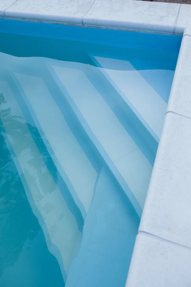 Escalones de acceso a una piscina con agua clara y azulada, lista para el baño