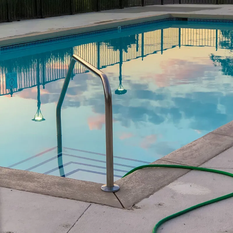 Piscina residencial al atardecer con una manguera sobre el borde de hormigón