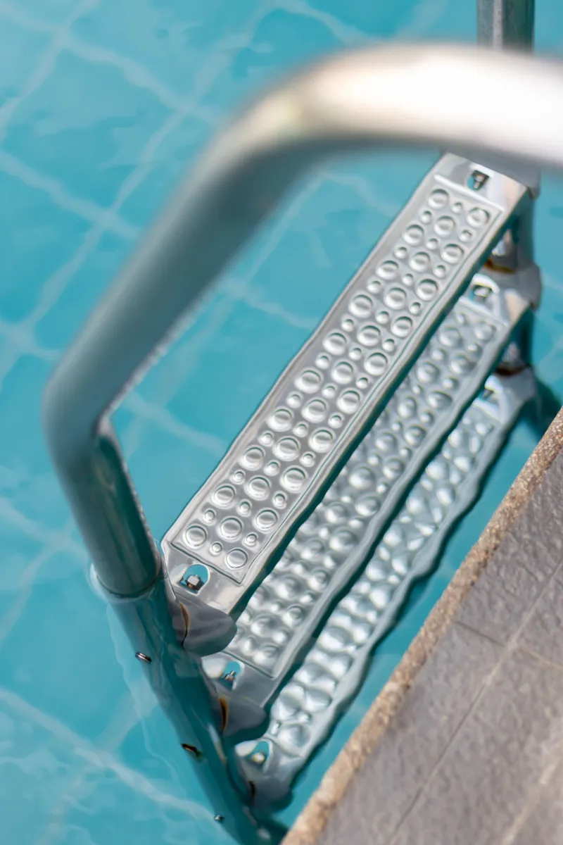 Escalera metálica sumergida en el agua transparente de una piscina bien mantenida