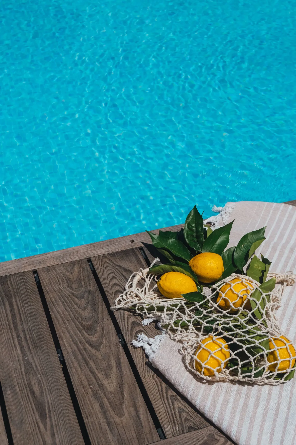 Piscina de agua turquesa junto a una tarima de madera con una bolsa de red