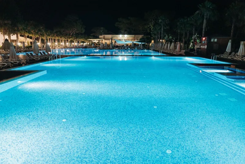 Piscina iluminada de tono turquesa al anochecer en una zona ajardinada
