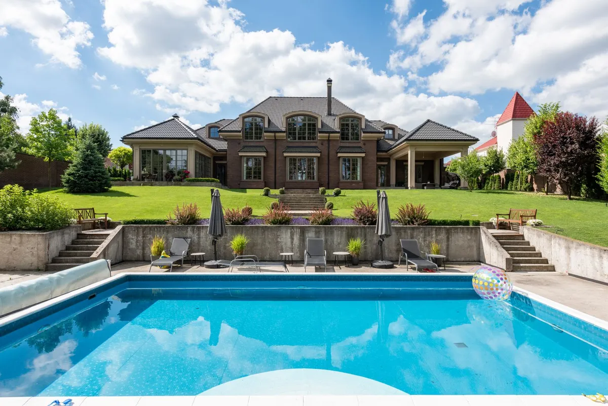 Amplia piscina exterior frente a una vivienda con jardín, en un día soleado de verano
